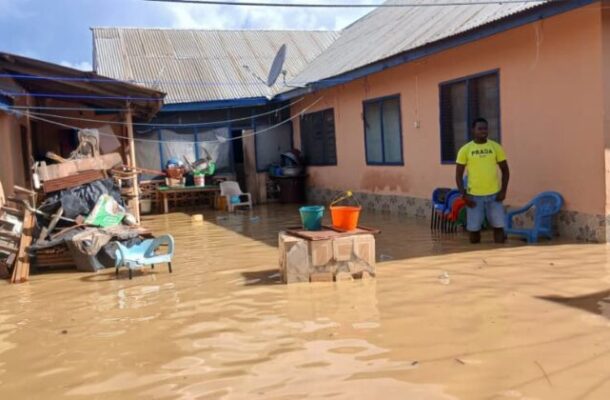 flood | Ghanaguardian.com Flooded courtyard of an orange house with muddy water covering the ground; a man in a yellow shirt stands near blue chairs while buckets sit on a table.