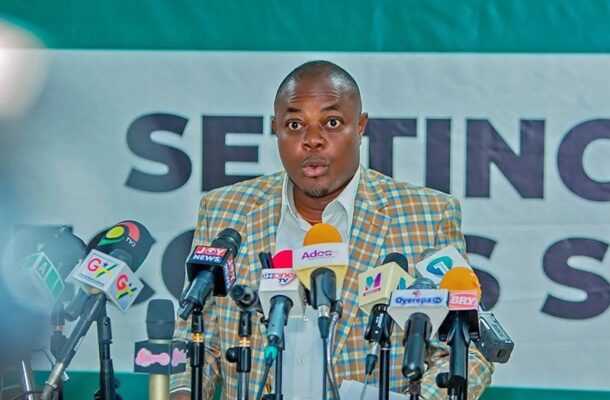 godwin | Ghanaguardian.com Man in a checkered blazer addresses a press conference, microphones from various outlets in front of him.