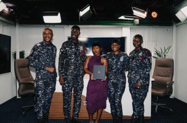 Group photo in a studio: four military personnel in camo uniforms and a woman in a purple dress holding a diploma.