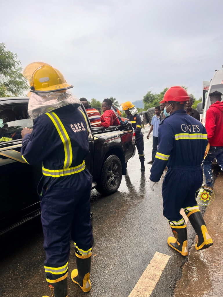 image-2922-769x1024-1 | Ghanaguardian.com Firefighters in blue uniforms with yellow stripes assist at a vehicle crash on a wet road, crowd gathered nearby.