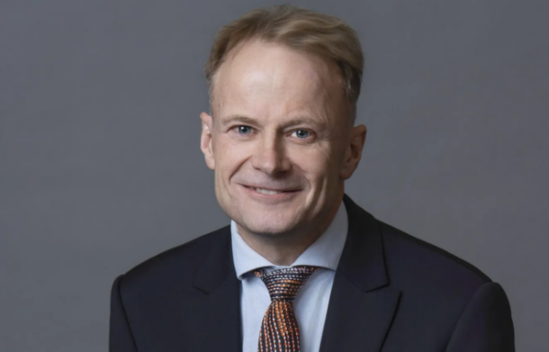 image-302-696x391 | Ghanaguardian.com Portrait of a smiling man in a dark suit and patterned tie against a gray background.