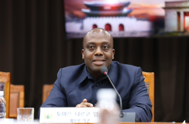 image-621-1024x682 | Ghanaguardian.com Man in a dark blue suit speaking at a panel with a microphone in front and a nameplate on the table