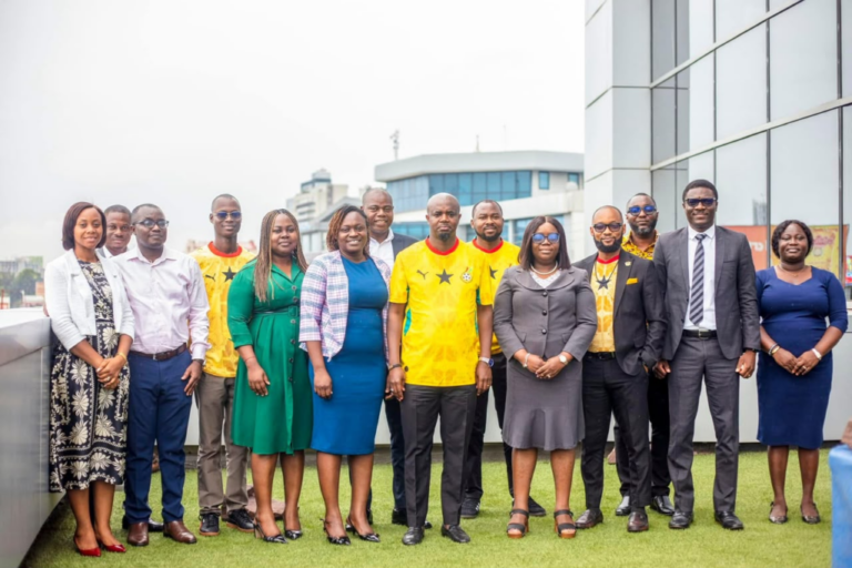 Diverse group of professionals posing on a rooftop terrace, some in yellow jerseys and others in business attire with city buildings behind.