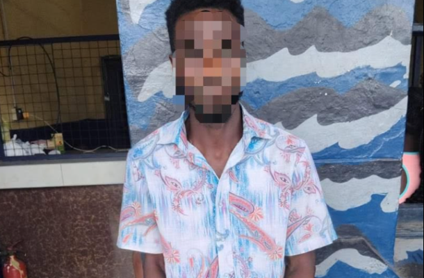 Man with short dark hair wearing a light blue floral shirt, standing in front of a blue wavy mural; face pixelated/blurred.
