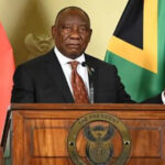 President delivering a speech at a wooden podium with the presidential seal; national flags behind him.