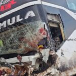 Bus with severe front-end damage and a shattered windshield from a crash, debris on the ground nearby, logos visible on the bus.