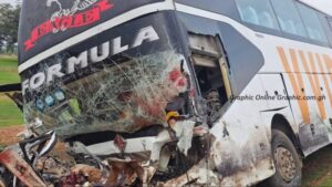 Bus with severe front-end damage and a shattered windshield from a crash, debris on the ground nearby, logos visible on the bus.