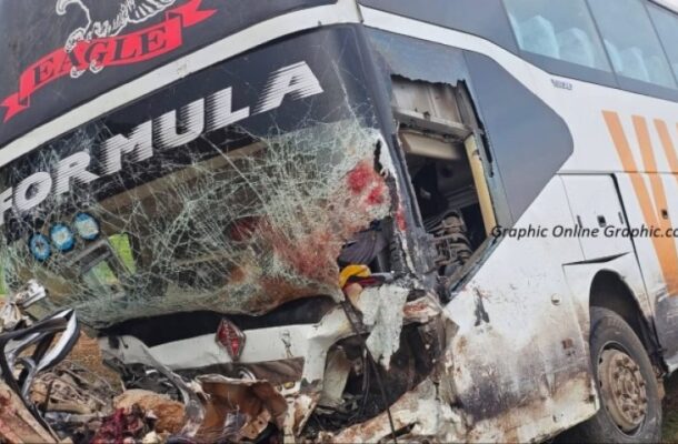 Bus with severe front-end damage and a shattered windshield from a crash, debris on the ground nearby, logos visible on the bus.