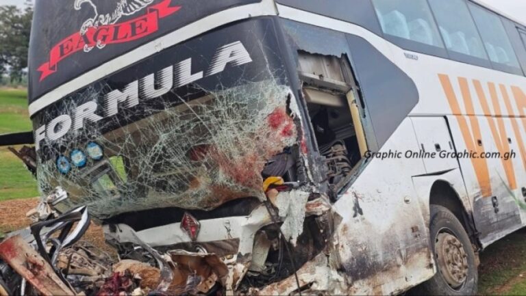 Bus with severe front-end damage and a shattered windshield from a crash, debris on the ground nearby, logos visible on the bus.