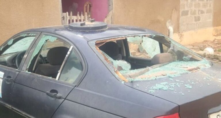 Blue sedan with a shattered rear window and broken glass on the back seat area.