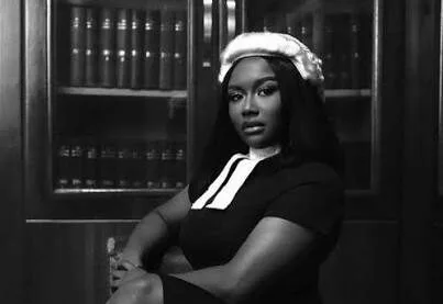 Black-and-white portrait of a Black woman wearing a white era wig and dark dress with a white collar, seated with arms crossed in front of a bookshelf filled with legal volumes.