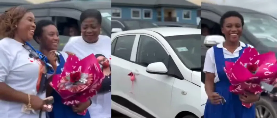 Group of women smiling outside a white car with pink ribbon; a student in blue and white holds a pink bouquet.