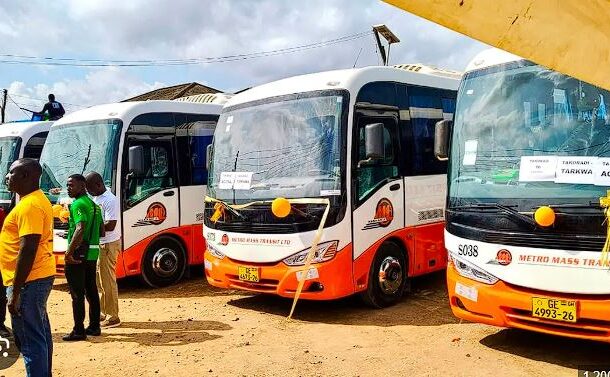 mass | Ghanaguardian.com Row of white-and-orange Metro Mass Transit buses parked on a dusty lot, with people standing nearby at what appears to a launch event.