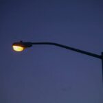 Streetlight with a warm yellow glow against a dark blue evening sky.