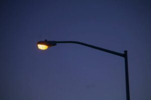 Streetlight with a warm yellow glow against a dark blue evening sky.