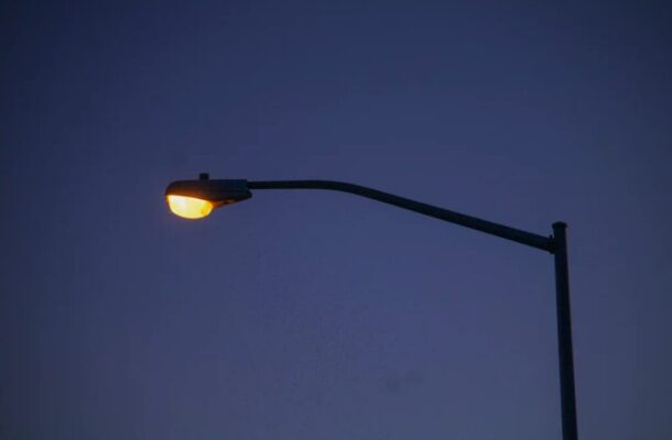 Streetlight with a warm yellow glow against a dark blue evening sky.