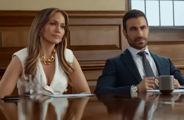 Two business professionals sit at a polished conference table in a wood-paneled room.