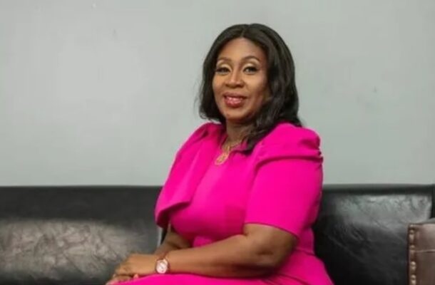 sedinam | Ghanaguardian.com Woman in a bright pink dress sits on a black leather couch, smiling at the camera.