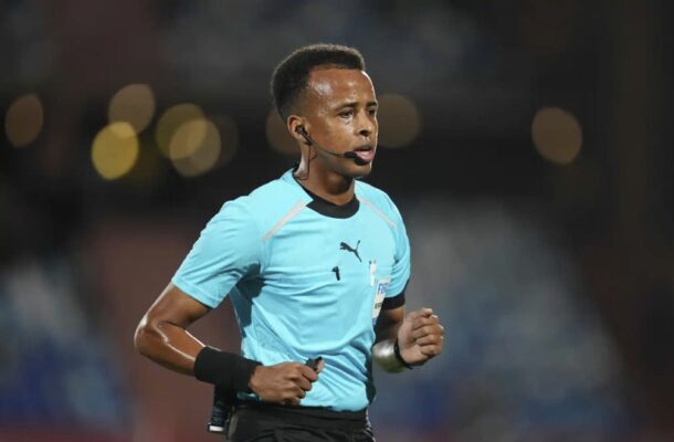 Soccer referee in a light blue uniform with a headset mic, running on the field during a match