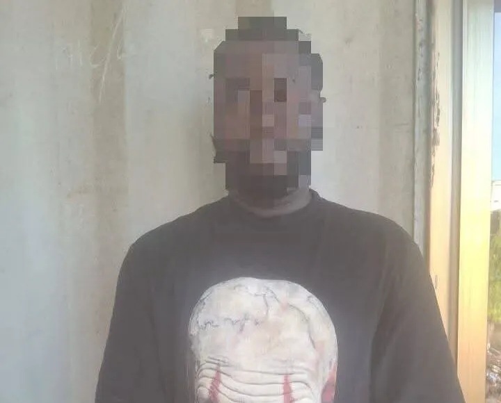 Man standing indoors against a concrete wall, wearing a black T-shirt with a large white skull graphic.