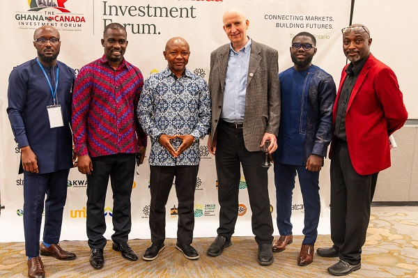Six men in smart casual attire posing for a photo at a Ghana Investment Forum event, standing in front of a banner with logos.