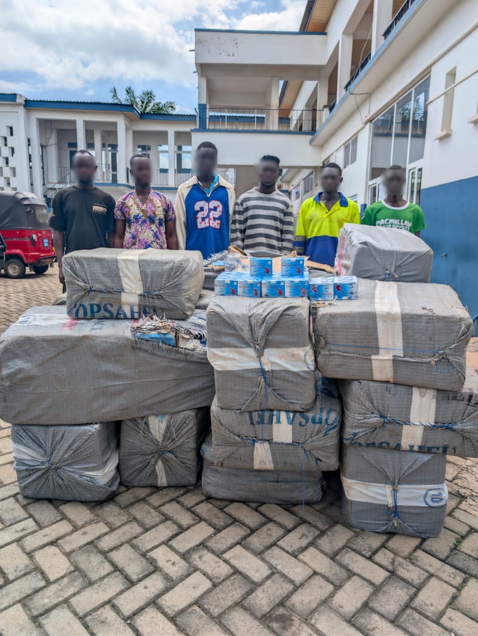 Group of people standing behind stacked wrapped shipments and boxes, ready for donation or delivery at a campus or facility courtyard.