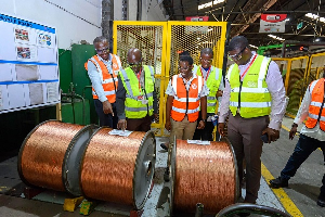 Group of workers in high-visibility vests observing large copper cable spools on the factory floor.