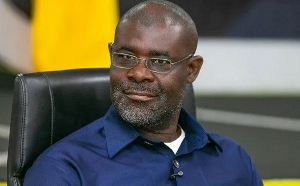 65799262295 | Ghanaguardian.com Man with glasses and a short beard, wearing a blue shirt, seated in a black chair on stage with a lavalier mic.