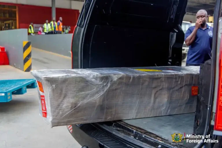 Large, plastic-wrapped pallet being loaded into the back of an SUV at a loading dock, with ministry logo visible in the corner.
