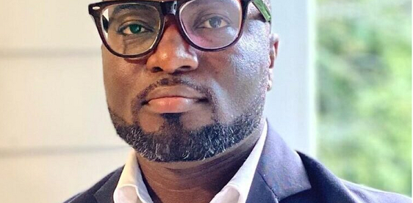 78592448 | Ghanaguardian.com Close-up portrait of a man wearing glasses, a white shirt, and a dark blazer, looking at the camera.