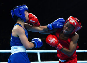 Two female boxers, one in blue and the other in red, exchange punches in a ring during a match in progress.