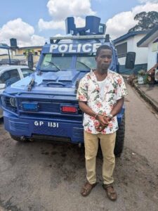 Man in floral shirt and sandals stands beside a blue police armored vehicle labeled POLICE with equipment on top.",