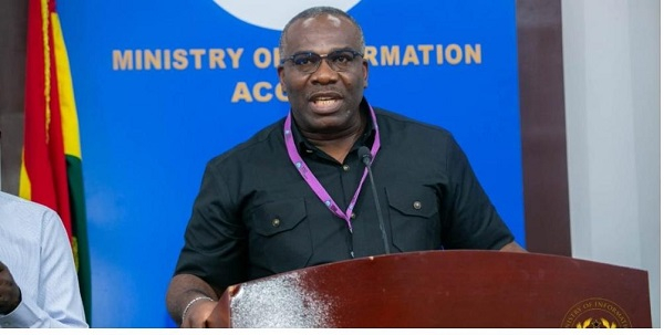 Edward E Obeng-Kenzo | Ghanaguardian.com Man speaks at a wooden podium during a Ministry of Information event, wearing a black shirt and a purple lanyard, with a blue backdrop behind him.