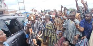 Crowd of people surrounding a man in traditional striped clothing stepping from a car; many hold up phones to take photos and videos.