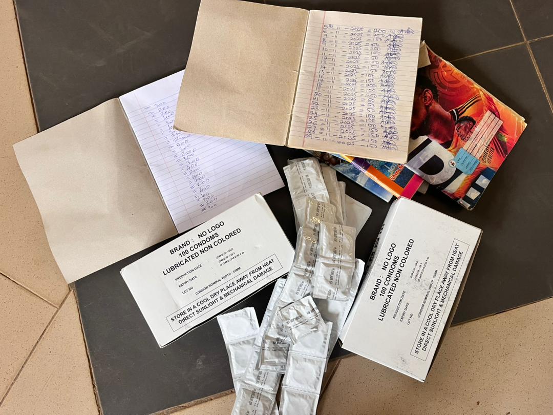 Assorted papers, notebooks, and condom boxes scattered on a floor, with loose condom wrappers among them.