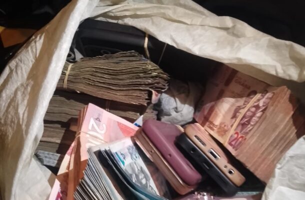 White bag filled with bundled banknotes and several mobile phones scattered inside.