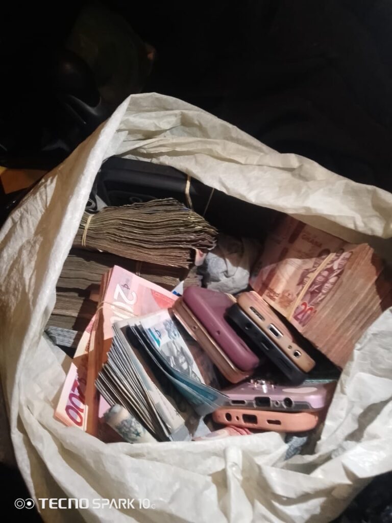 White bag filled with bundled banknotes and several mobile phones scattered inside.