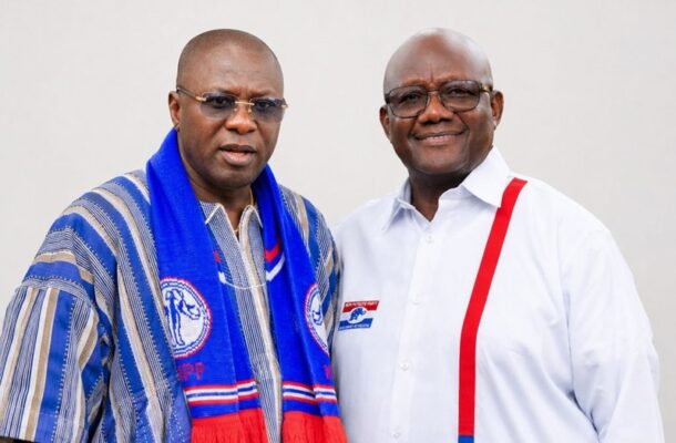 IMG-20260701-WA0026 | Ghanaguardian.com Two men posing for a photo, one in a blue scarf with party logos and the other in a white shirt with red suspenders and a campaign badge.