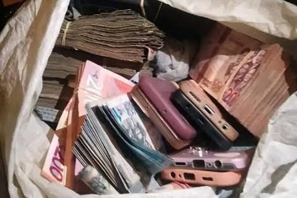 A white bag filled with stacks of cash and several old mobile phones piled inside.