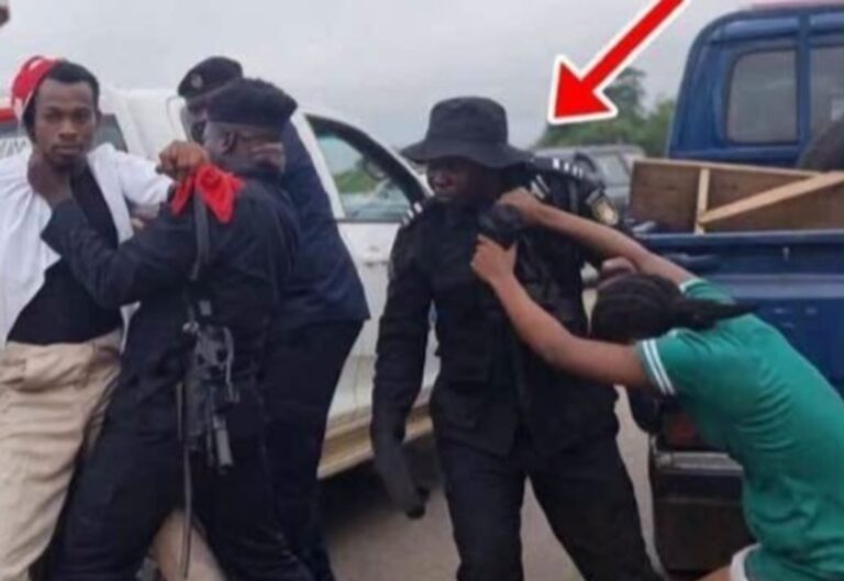 Group of men restraining a person near a pickup truck; an armed officer in black watches, with a red arrow highlighting the scene.