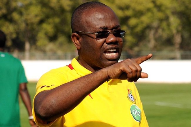 Man in a yellow polo with sunglasses on a soccer field, gesturing and pointing while speaking.
