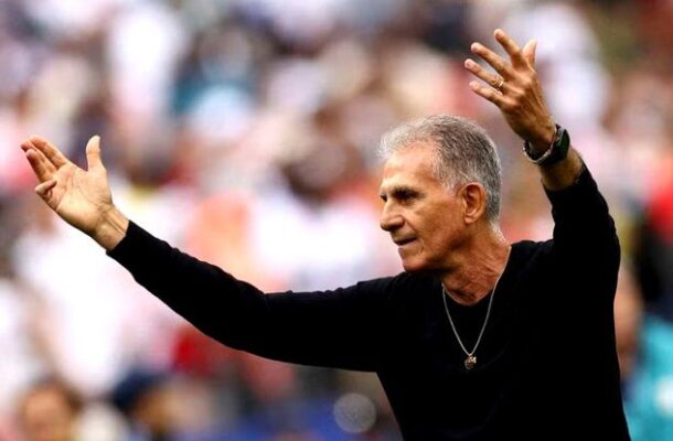 Man with gray hair in a black shirt raises his arms in celebration at a packed stadium.