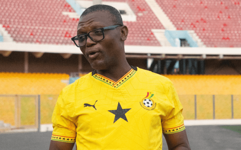 Man wearing a bright yellow football jersey with a black star, standing on a stadium field and talking.