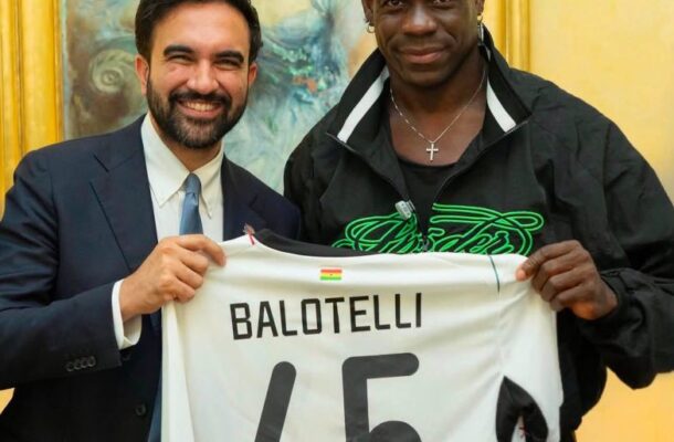 IMG_1138 | Ghanaguardian.com Two men smile while holding a white soccer jersey that reads BALOTELLI 45, with a small flag, in front of a gold-framed painting.