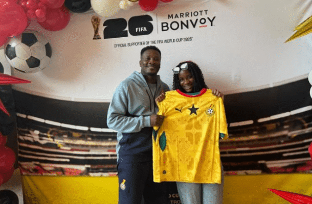 IMG_1141 | Ghanaguardian.com Two people pose indoors with a yellow soccer jersey, in front of a FIFA World Cup 2026 Bonvoy backdrop with balloons nearby.
