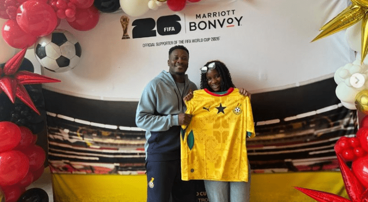 Two people pose indoors with a yellow soccer jersey, in front of a FIFA World Cup 2026 Bonvoy backdrop with balloons nearby.