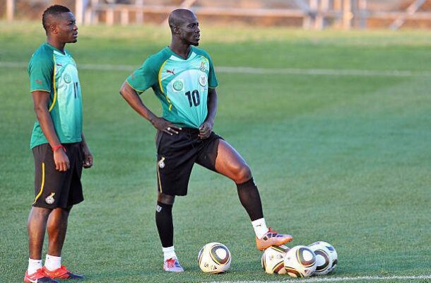 Two soccer players in green training kits stand on a grass field with several soccer balls at their feet.