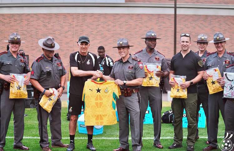 Group of uniformed officers on a football field presenting yellow jerseys to each other during a ceremony.