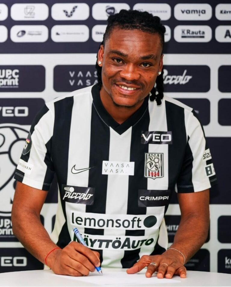 Athlete in a black-and-white striped jersey signs a document at a table during a press event, with sponsor logos in the backdropsmiling at the camera.