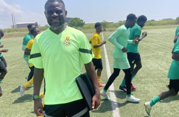 IMG_1167 | Ghanaguardian.com Coach or trainer standing on a sunny soccer field with a clipboard, surrounded by players in neon green jerseys warming up on artificial turf